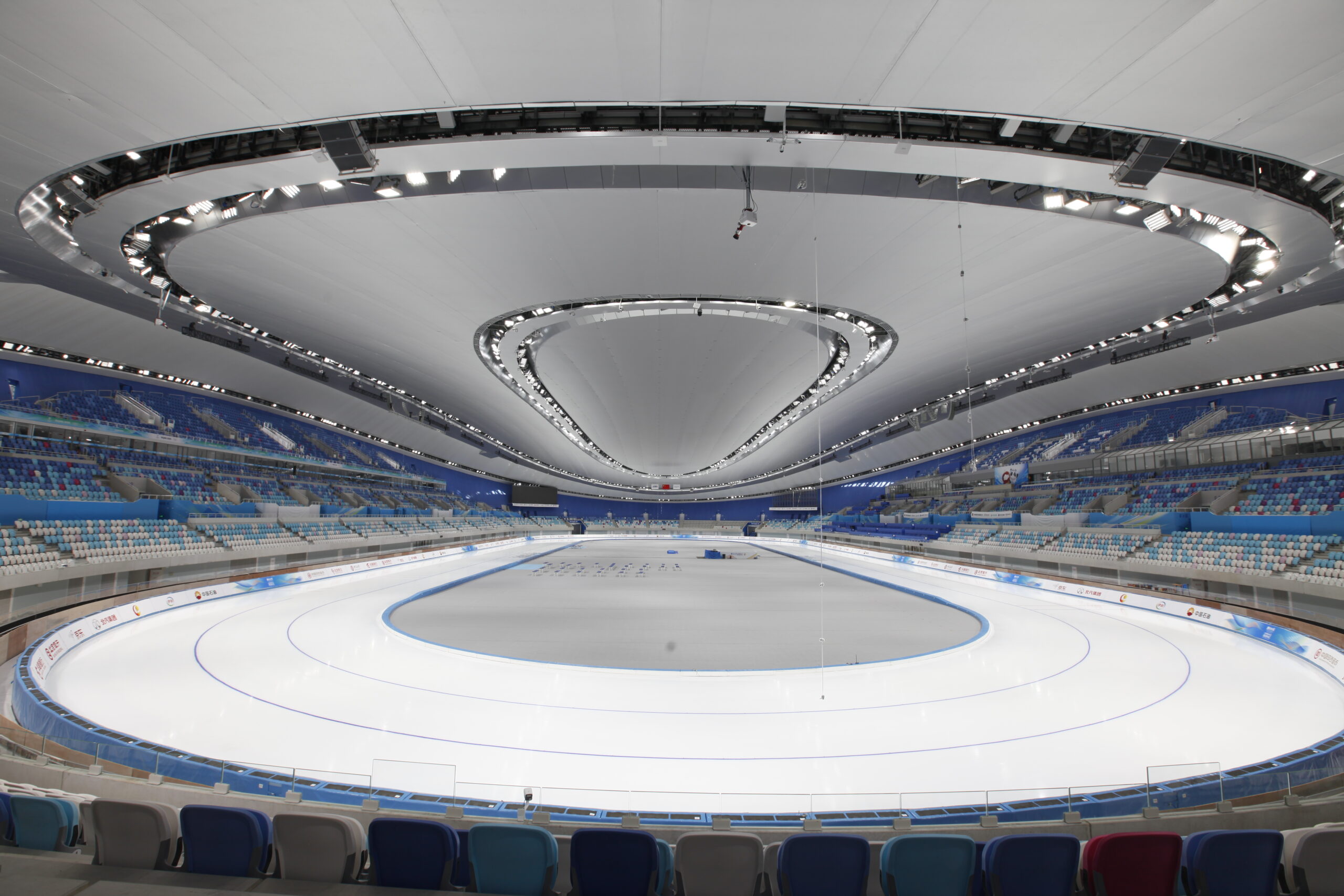 A view of the inside of the National Speed Skating Oval, showcasing the speed skating tracks, bleachers, and distinctive ceiling