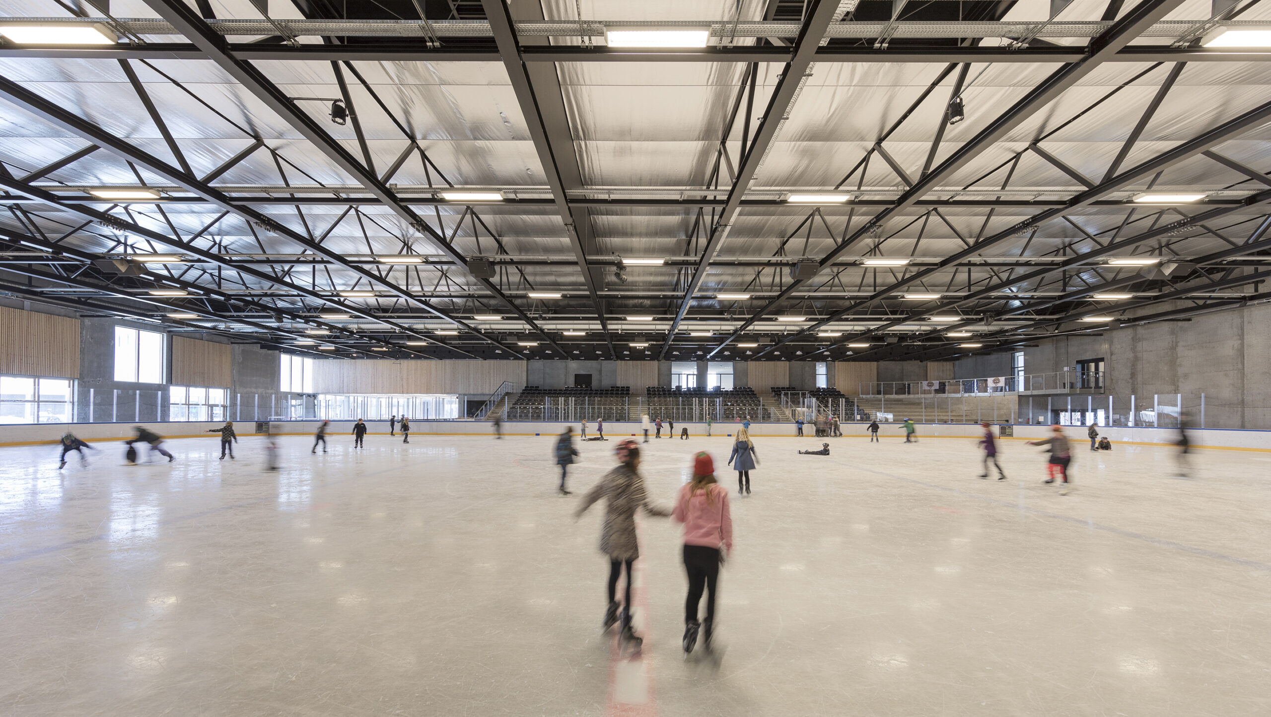 Skaters glide across the Ørestad Ice Rink, as expansive windows reveal the surrounding outdoor scenery.