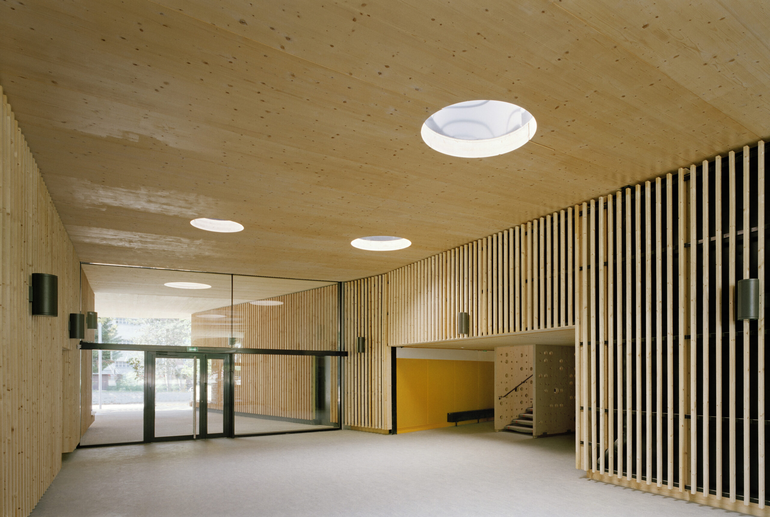 An interior shot of the warm and inviting wooden entrance of the school, featuring wooden cladding and ceiling, which is further accentuated by innovative circular skylights