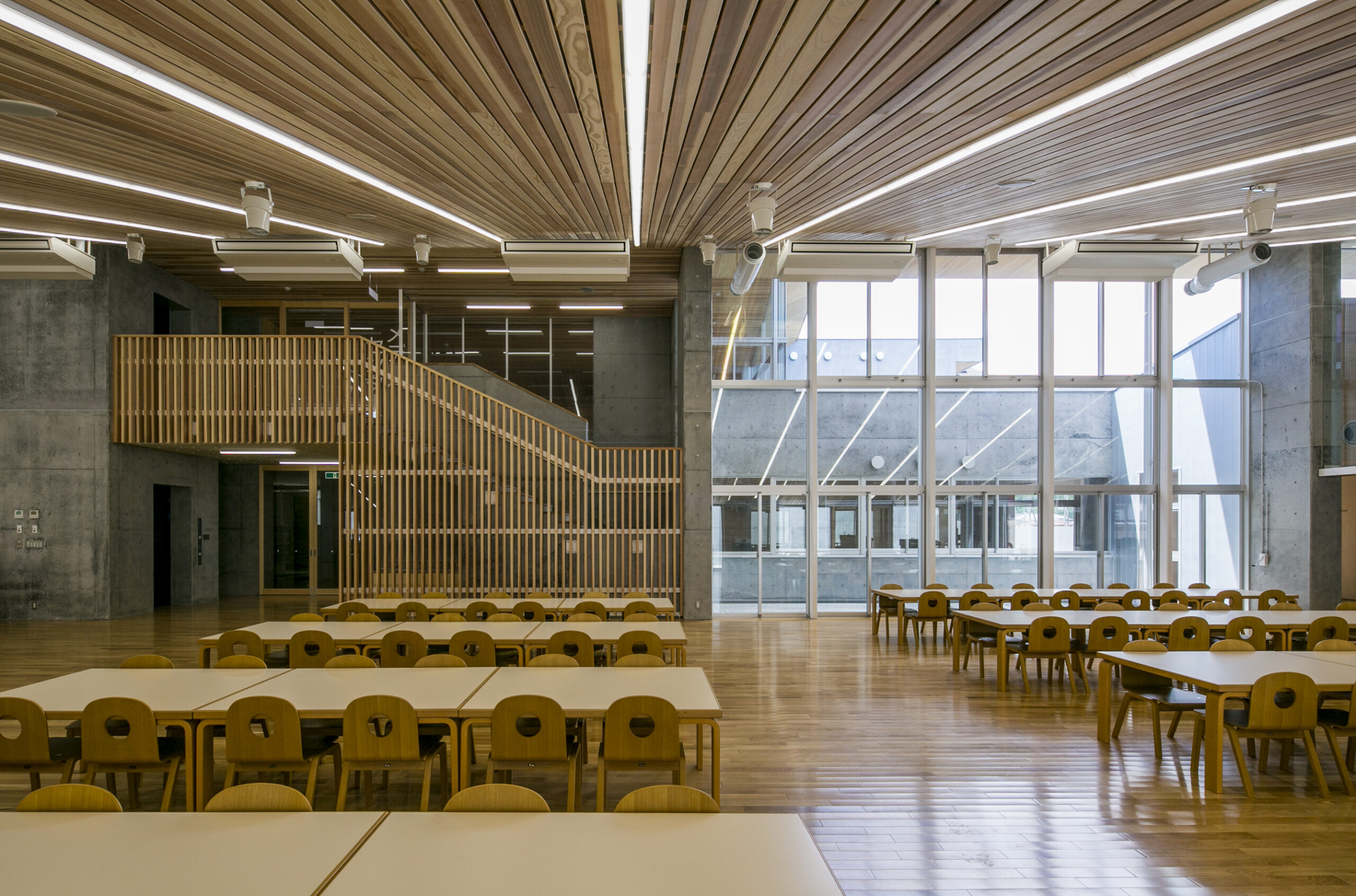 A two-storey common area of the school, seamlessly blending the natural warmth of wooden ceilings and floors with the sleek and modern aesthetic of concrete walls. 